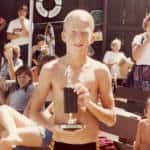 Boy holding a trophy at a summer outdoor event, surrounded by people watching.