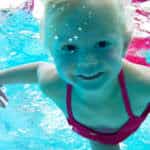 Young girl in a pink swimsuit swimming underwater, smiling at the camera.