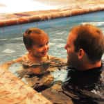 A man and a young child smiling at each other while in a swimming pool.