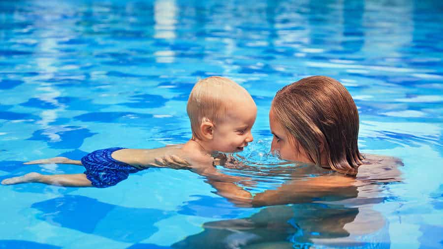 A woman and a baby smiling at each other while swimming in a crystal clear pool.