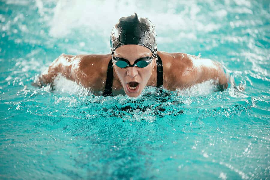 Female swimmer in goggles and cap executing the butterfly stroke in a pool.