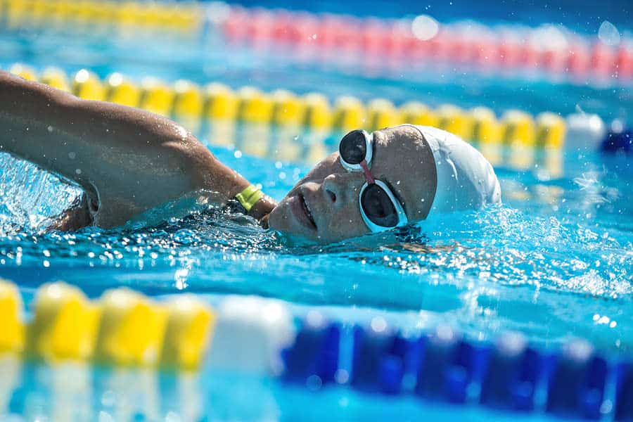 Swimmer in goggles and cap performing backstroke in a pool with clear blue water and lane markers visible.