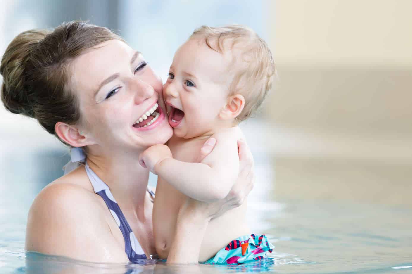 A joyful mother holding her laughing baby in a swimming pool at Huntington Beach.