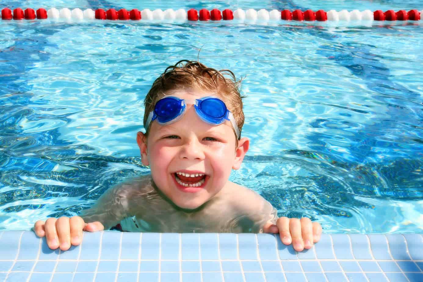 Young boy with goggles smiling at the edge of a swimming pool in Newport Beach.