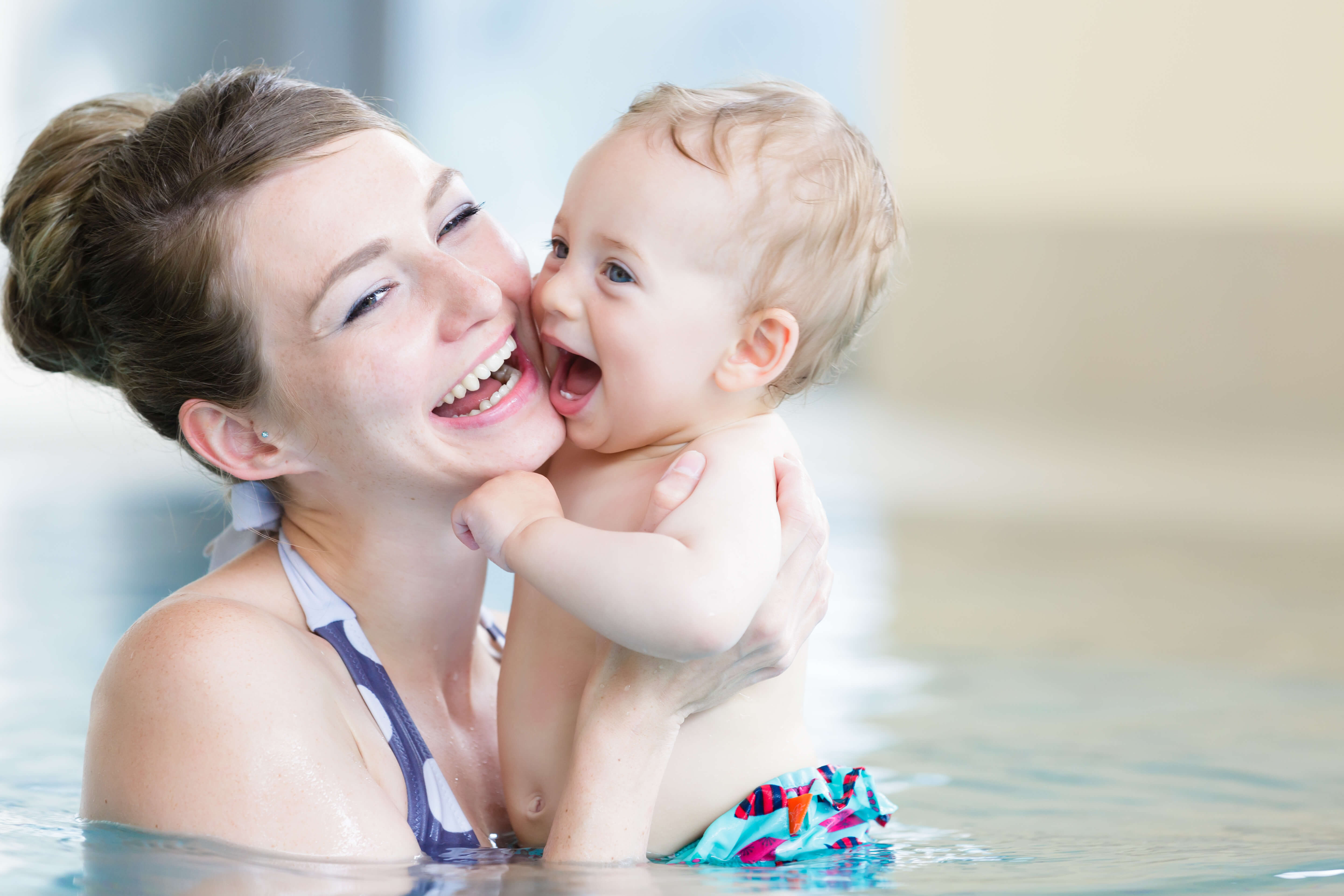 A joyful young woman holding a laughing baby while they are both in a swimming pool in Tustin.