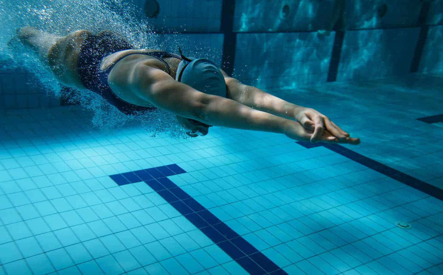 A swimmer dives underwater in a pool, showcasing a streamlined posture with arms outstretched.