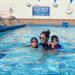 A swimming instructor with two children wearing goggles in a pool at blue buoy family swim school.