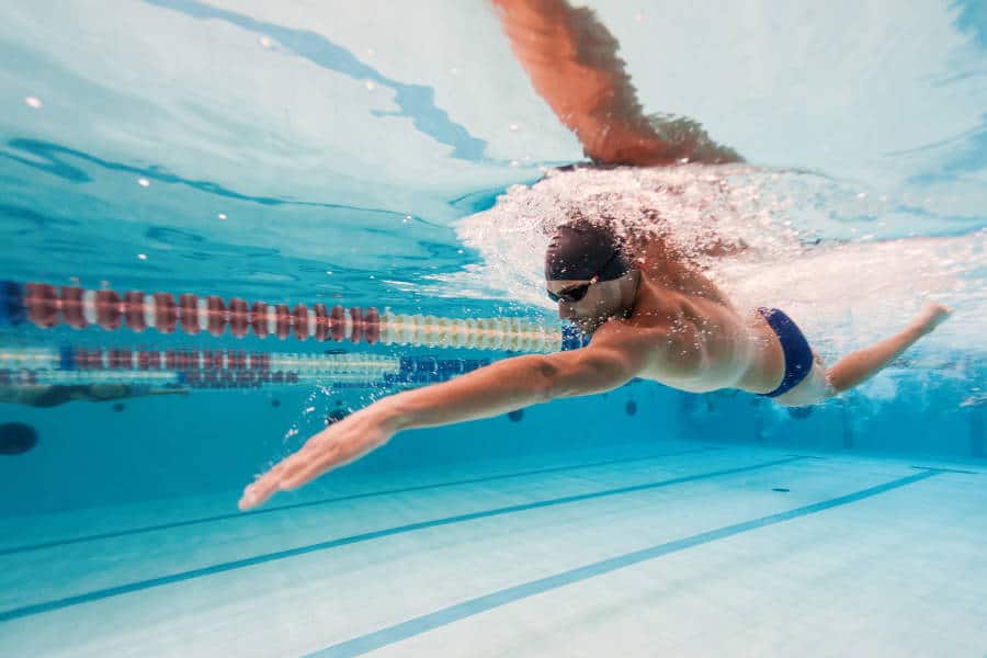 Underwater view of a swimmer in a blue swimsuit reaching forward mid-stroke in a clear pool, with strong focus on the movement and bubbles.