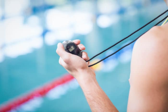 A swimmer holding a stopwatch at the edge of a pool, focusing on timing their training session.
